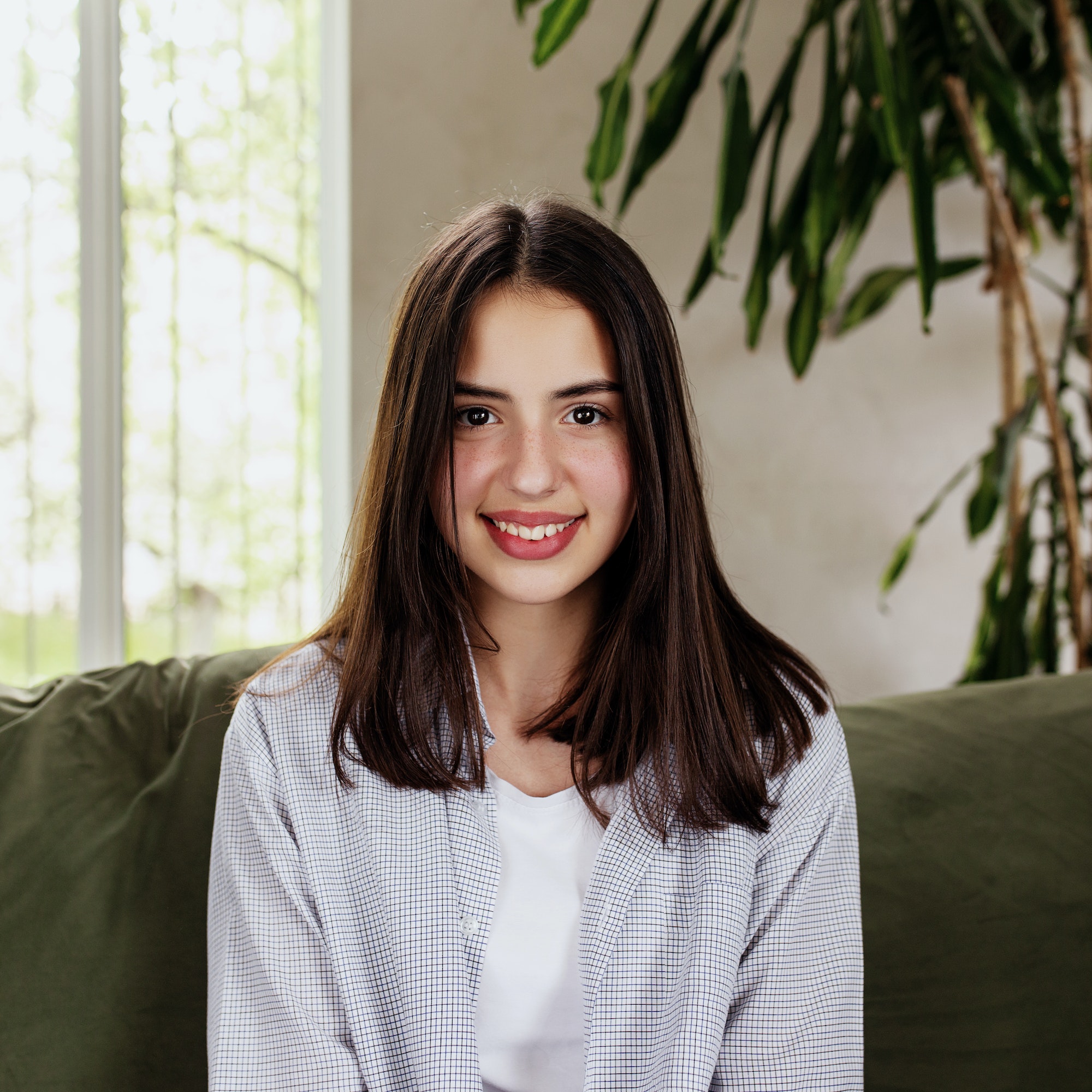 Beautiful smiling caucasian girl sitting at green sofa and watching at camera